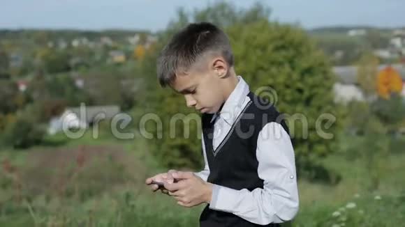 男孩站在户外玩手机视频的预览图