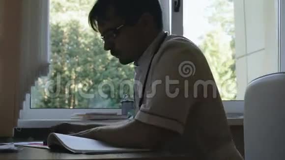 一位医生坐在靠窗的桌子旁的剪影视频的预览图