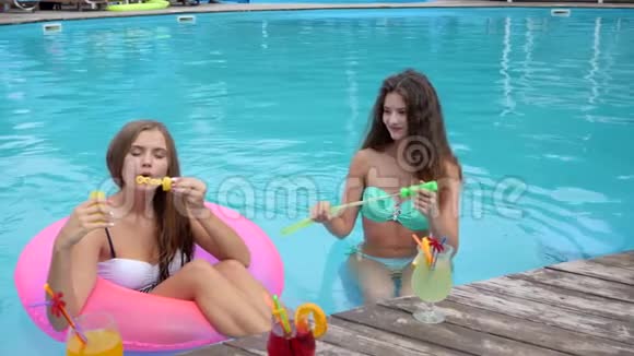 穿着泳衣的女朋友在泳池边吹肥皂泡可爱的女孩坐在泳池里的充气圈里做视频的预览图