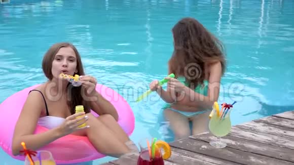 鸡尾酒会女朋友穿着泳衣在游泳池里吹肥皂泡朋友陪伴在池边放松视频的预览图