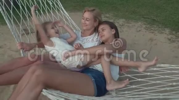 小女孩轻轻地抱着妈妈和妹妹在吊床上慢动作股票录像视频的预览图