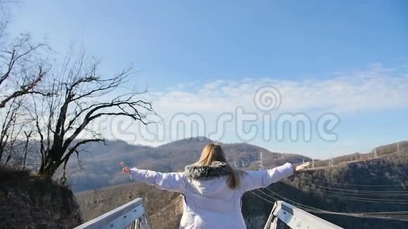 年轻开朗的女人在美丽的山顶前的天空桥上举起双臂在金色的夕阳天空中视频的预览图