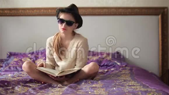 戴着太阳镜戴着帽子的小女孩看着照相机看书微笑视频的预览图