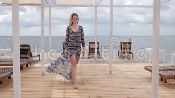 戴眼镜的女士光着脚在海边的码头上散步视频的预览图