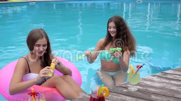 夏天的聚会女朋友穿着泳衣在泳池边吹肥皂泡可爱的女孩坐在泳池的充气圈里视频的预览图