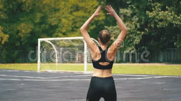 在公园运动场上从事健身运动的年轻运动员女子的后景视频的预览图