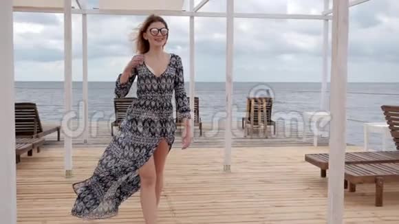 年轻女子赤着脚走在木墩上戴眼镜的女士赤着脚走在海边的码头上视频的预览图