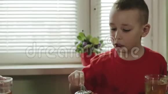 一个穿着红色t恤的小男孩正在桌旁吃蛋糕喝茶视频的预览图