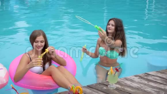 可爱的女孩坐在游泳池里的充气圈里做泡泡夏天的聚会穿着泳衣的朋友休息视频的预览图