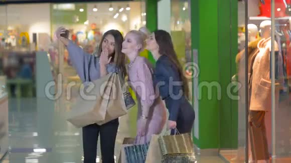 三个漂亮的年轻女孩拿着购物袋拍照自拍女孩们笑着笑着看着视频的预览图
