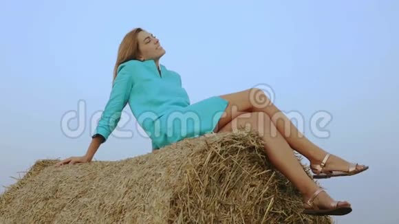 迷人的女人坐在蓝天背景下的干草堆上视频的预览图