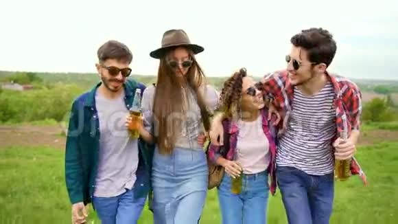 四个时髦的快乐嬉皮士正拿着瓶啤酒在公园里散步拥抱在一起视频的预览图