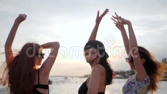 女孩们在河堤上玩得很开心最好的女朋友在海滩上的日落中跳舞三个女人在海边举起手臂视频的预览图