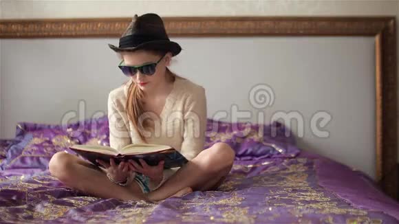 戴太阳镜戴帽子的小女孩看书看相机翻页视频的预览图