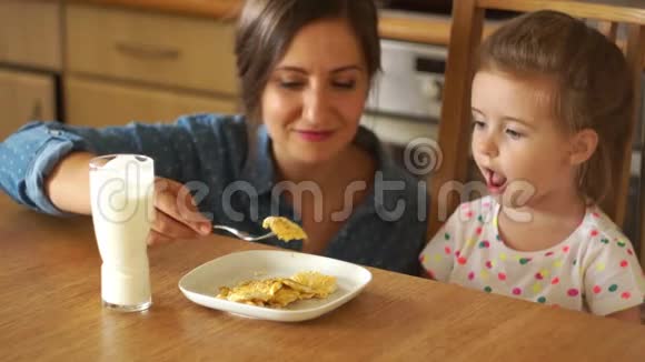 妈妈喂她的小女儿女孩顺从地张开嘴炒鸡蛋健康早餐婴儿食品视频的预览图