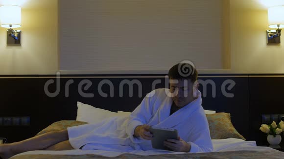 一个年轻人躺在酒店的床上看着手机平板电脑视频的预览图