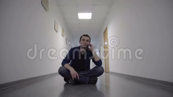 男人坐在长长的白色走廊上用手机说话视频的预览图