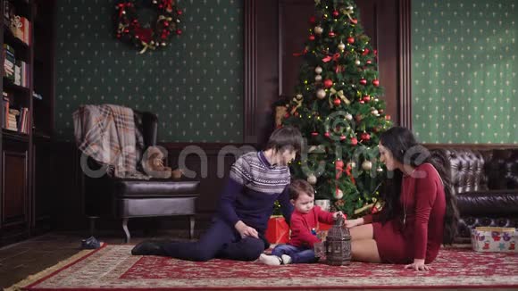 可爱的一家人在除夕坐在美丽的圣诞树旁边的地毯上视频的预览图