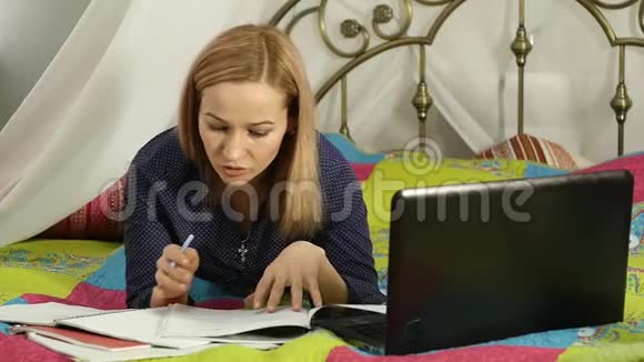 学生躺在家里的床上在笔记本电脑上工作的女人在线教育慢动作视频的预览图