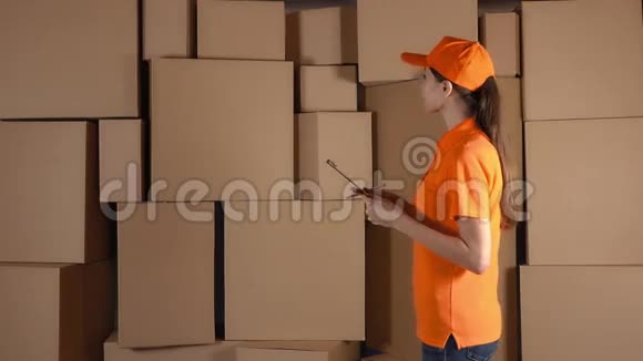 女仓库工人穿橙色制服计数箱并对棕色纸箱做记录4K工作室照明视频的预览图