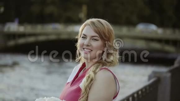 可爱的金发女郎穿着红色连衣裙住在河堤上视频的预览图