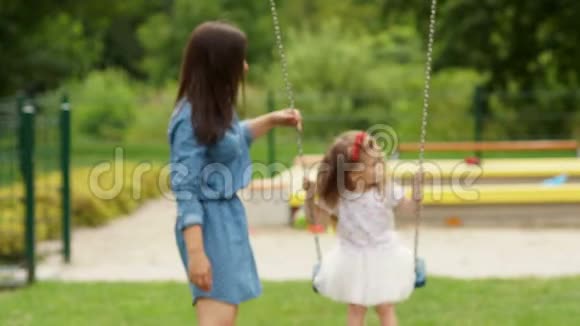 漂亮的布鲁内特和她可爱的女儿在游乐场玩耍的肖像小女孩骑着秋千出门视频的预览图