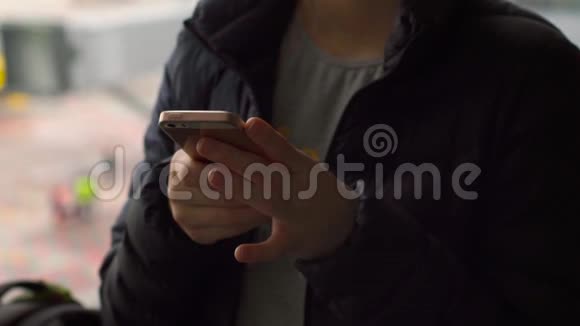 一名年轻女子在机场一扇大窗户前使用智能手机的特写镜头视频的预览图