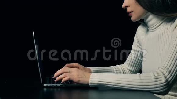 漂亮的黑发女人在黑色背景下的便携式电脑上打字4K视频视频的预览图