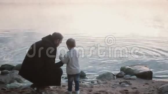 父子两人上岸小男孩扔石头下水男人蹲着教男孩如何玩石头跳绳视频的预览图
