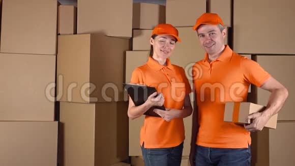 穿着橙色制服的男性和女性快递员站在棕色纸板箱周围送货公司工作人员4K视频的预览图