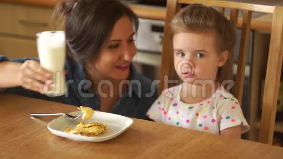 宝贝和凯菲尔一起吃早餐她嘴唇上有一个白色的胡子妈妈和女儿在厨房里笑视频的预览图