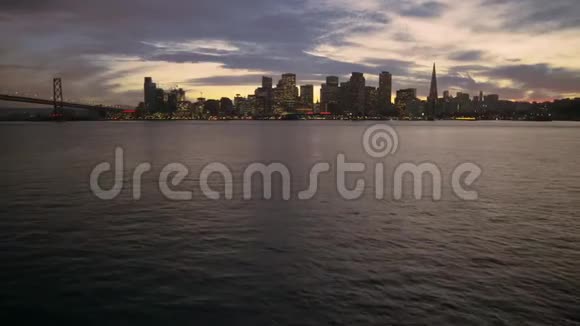 令人难以置信的空中无人驾驶飞机飞越平静的大洋河在旧金山黄昏的灯光下市中心的天际线日落的城市景观视频的预览图