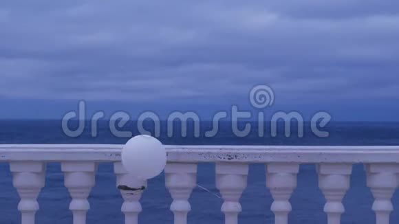 一个阴天白色气球在风中系在海边的栅栏上视频的预览图