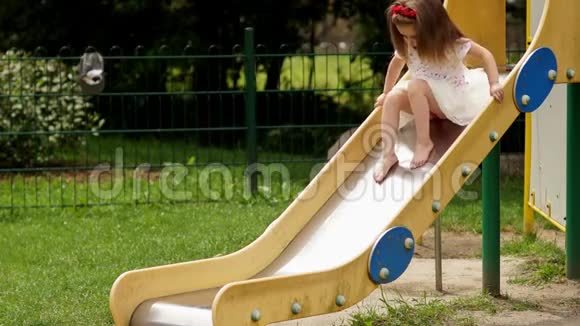 户外可爱的小女孩在夏日阳光明媚的日子里在游乐场的儿童滑梯上玩耍的肖像视频的预览图