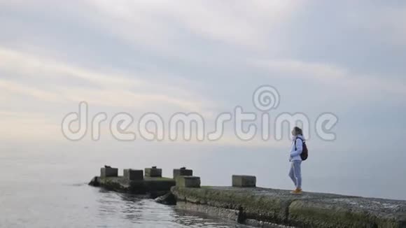 穿着夹克的女人站在海上码头环顾四周欣赏风景视频的预览图