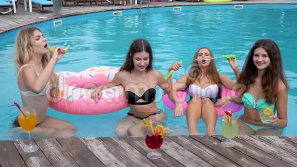 穿着泳衣的漂亮女孩们在游泳池里休息朋友们在游泳池边放松和泡泡视频的预览图