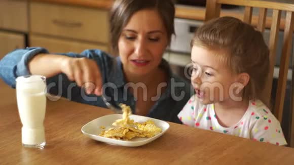美丽的黑发正在喂养她的女儿女孩张开嘴妈妈笑了炒鸡蛋和牛奶视频的预览图