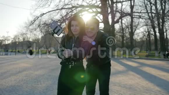 情侣在手机小玩意上自拍手机上自粘时尚男女孩在公园散步视频的预览图