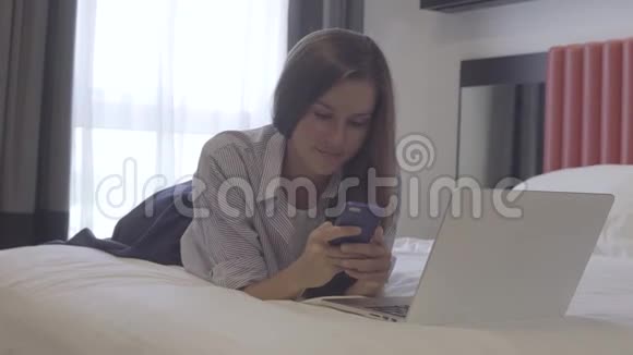 工作在智能手机和笔记本电脑上的女人躺在床上在线商务视频的预览图