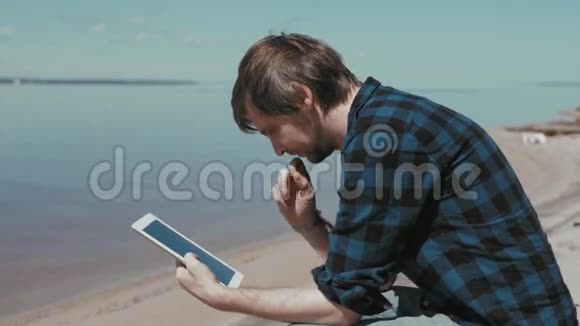 商人坐在海滩上用平板电脑工作学生在海边视频的预览图