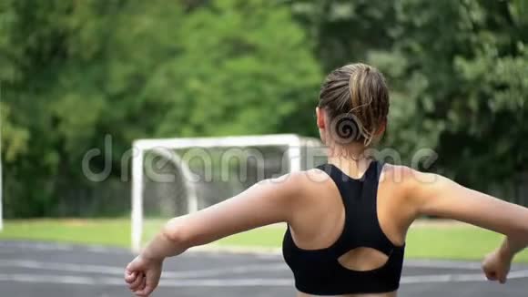 在公园的运动场上从事健身运动的年轻运动员女子的后景视频的预览图