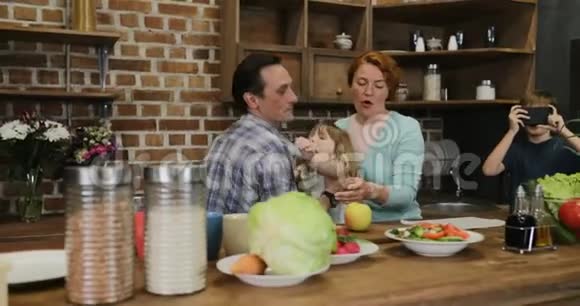 幸福的一家人在厨房做饭而儿子则在拍摄父母和姐姐一起做饭的视频视频的预览图