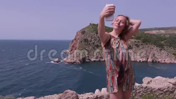 穿着裙子在海边摆姿势的女孩红头发做自拍手机风日视频的预览图