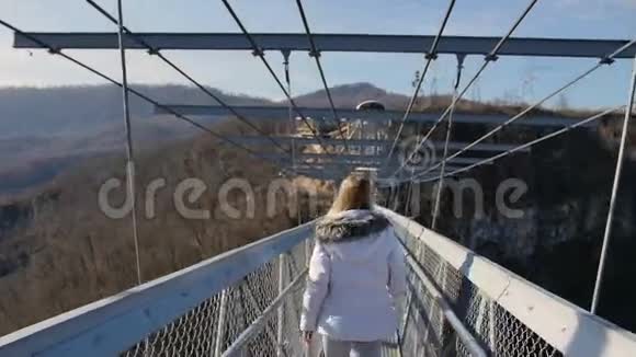 女人走过峡谷上的高桥手势跟着我视频的预览图
