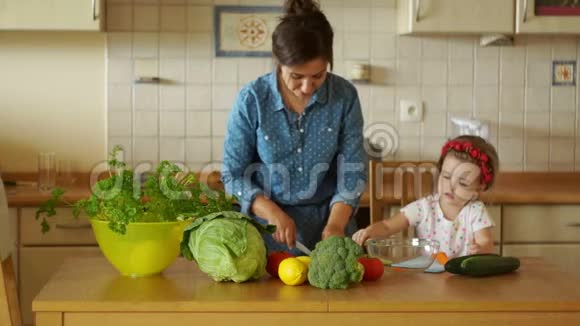 一位年轻的母亲正在厨房准备晚餐她切胡萝卜一个小女儿帮助我妈妈女孩视频的预览图