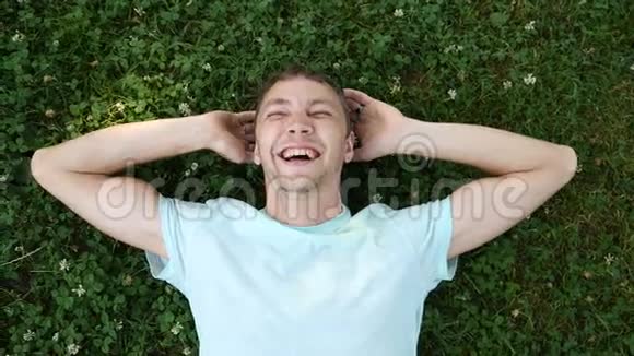 年轻的帅哥躺在夏天公园的草地上笑着看着镜头慢动作视频的预览图