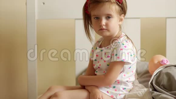 严肃的孩子看着相机坐在床上她身后是她的洋娃娃最喜欢的玩具特写肖像视频的预览图