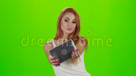 红头发的模特在一台平板电脑上做鬼脸绿屏工作室视频的预览图