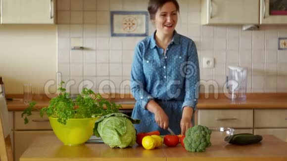 一个年轻的黑发女人正在切蔬菜做沙拉他尝试胡萝卜跳得很有趣我们自己做饭家庭烹饪视频的预览图