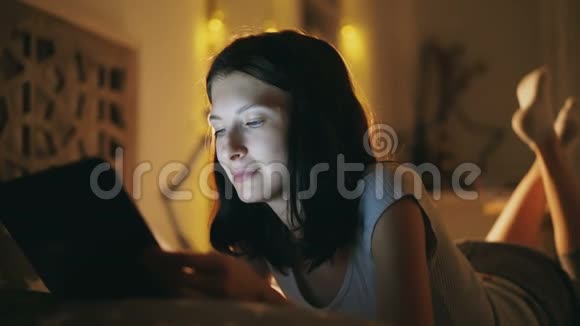 晚上躺在家里的床上用平板电脑为年轻漂亮的女人做特写视频的预览图
